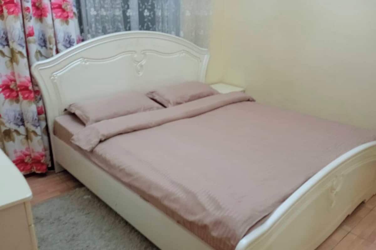 A neatly made bed with a white headboard and a beige bedspread.