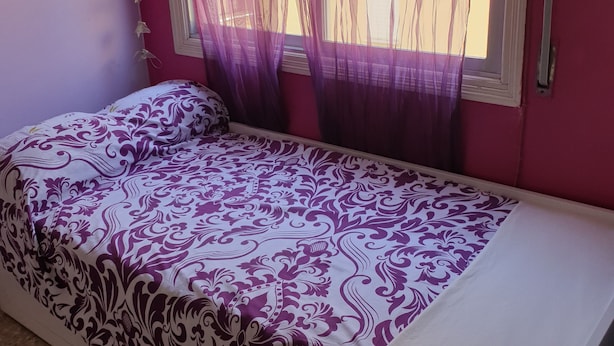 Una cama individual con una colcha estampada en una habitación con cortinas traslúcidas en la ventana.