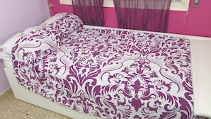 Una cama con una colcha estampada, una ventana con cortinas y una pared rosa.