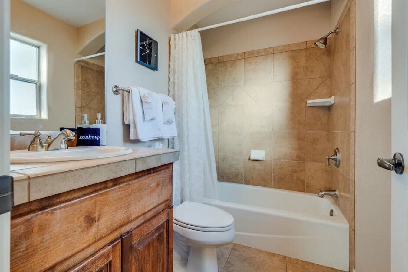 Une salle de bain avec un meuble-lavabo en bois, des toilettes blanches, une baignoire et un rideau de douche.