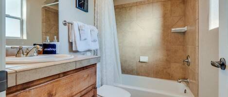 Une salle de bain avec un meuble-lavabo en bois, des toilettes blanches, une baignoire et un rideau de douche.