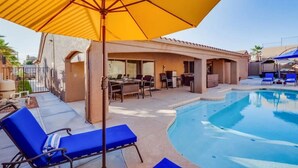 A pool area with blue lounge chairs, a yellow umbrella, and a covered seating area with tables and chairs. - Havasu Cabana - Pool, Spa, Games, Lake View, Garage (Lake Havasu City)