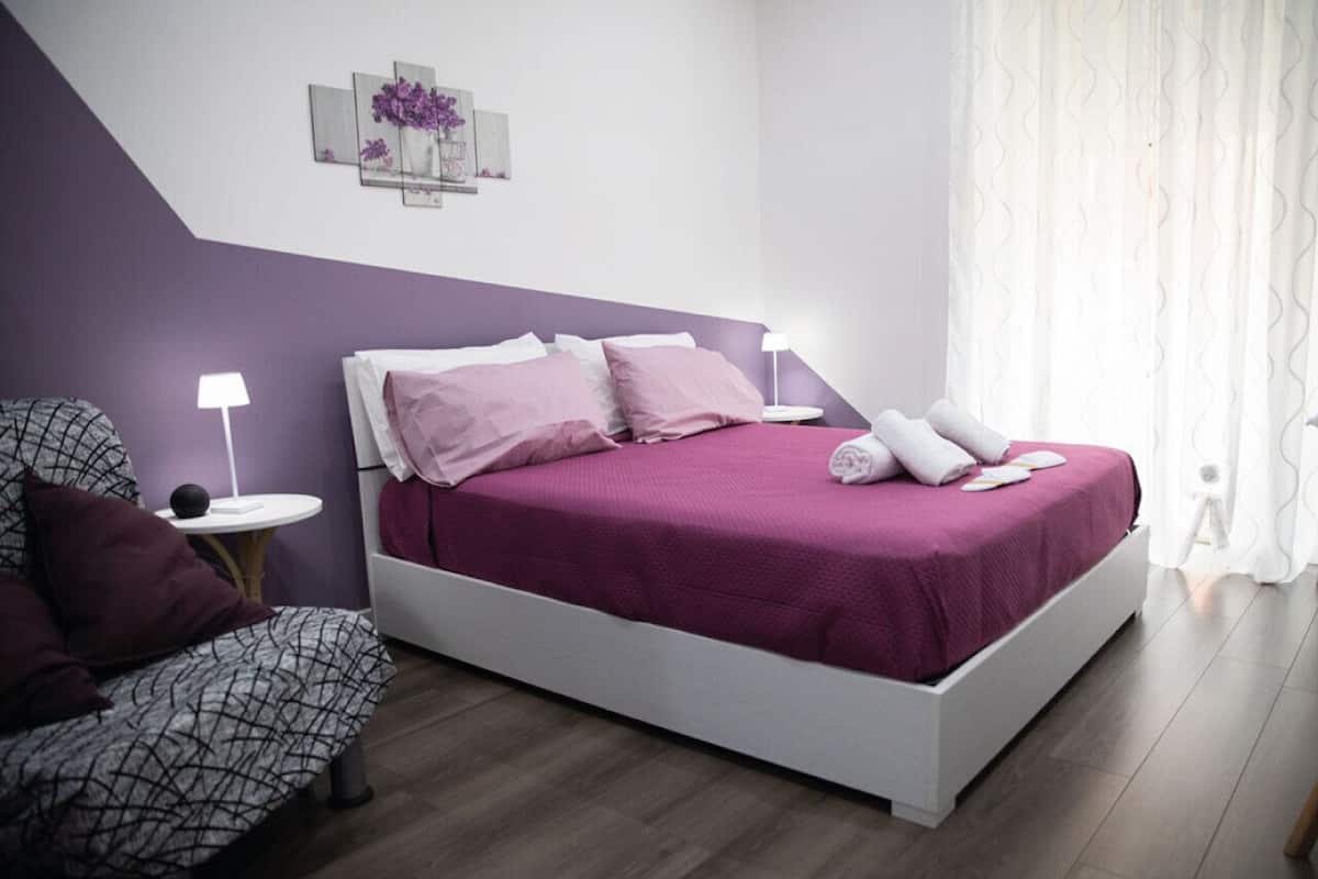 A bedroom with a bed, a chair, a bedside table, and a lamp.