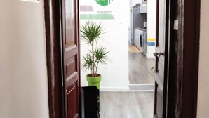 A hallway with a wooden door, a green potted plant, a doormat with "hello" and paw prints, and a sign with a logo and text. - Napoli Botanik Bed and Breakfast (Naples)
