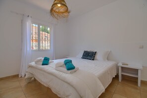 Une chambre à coucher avec un lit, une table de chevet, une fenêtre avec des rideaux et un luminaire suspendu.
