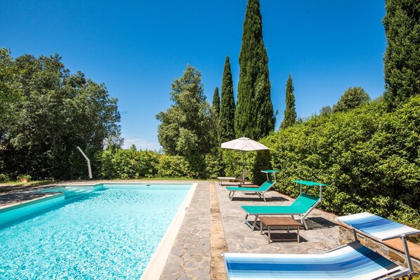 A swimming pool with lounge chairs and a stone pathway. - Podere Giardino Wine & Bed – Melograno Apartment: Country House with Pool, Wi-Fi & AC (Montalcino)