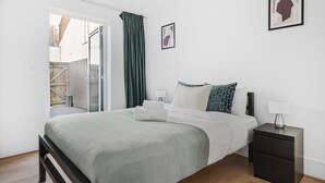 A bedroom with a bed, bedside tables, a window with curtains, and a view of the outside. - King's Cross Apartment with Terrace (London)