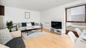 A modern living room with a sofa, coffee table, TV, and dining area. - King's Cross Apartment with Terrace (London)