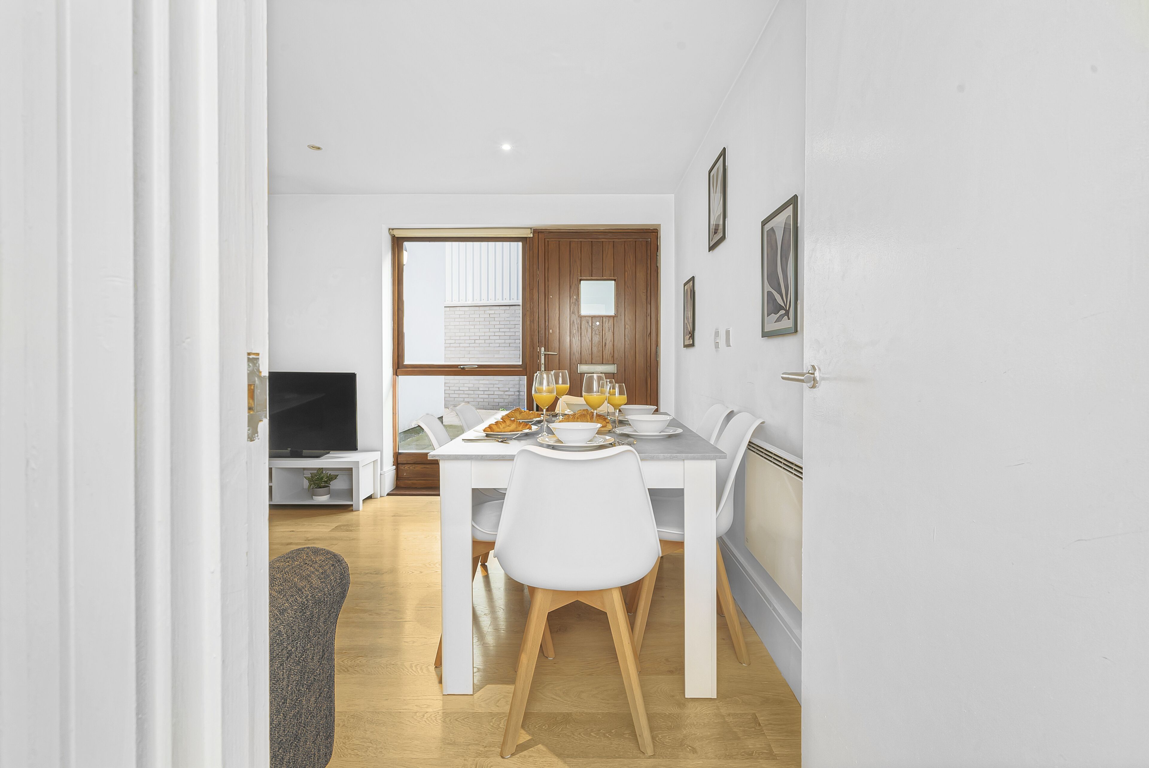 A modern kitchen with white cabinetry, a dining table set for four, and a television in the background.