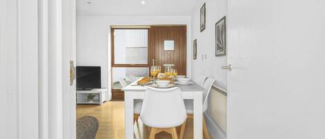 A modern kitchen with white cabinetry, a dining table set for four, and a television in the background.