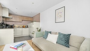 A modern living room with a beige sofa, a small coffee table, and a kitchen in the background. - King's Cross Apartment with Terrace (London)