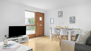A modern living room with a flat-screen TV, a dining area with a white table and chairs, and a grey sofa. - King's Cross Apartment with Terrace (London)