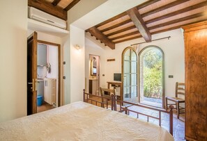 Un dormitorio con cama, vigas de madera, radiador, espejo, escritorio y vistas a vegetación.
