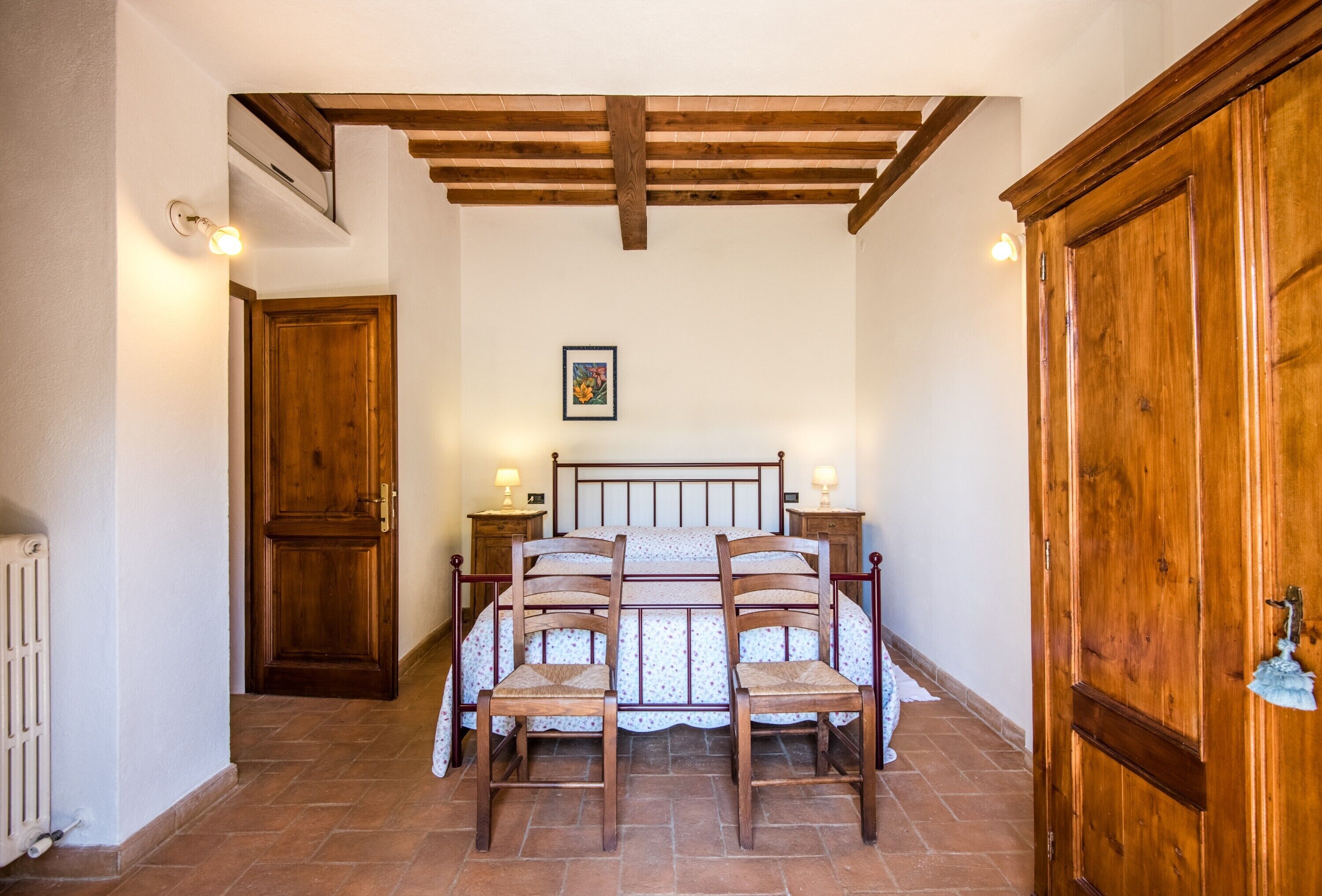 Quarto com estrutura de cama de madeira, duas mesas de cabeceira com luminárias, um radiador e um guarda-roupa de madeira grande.