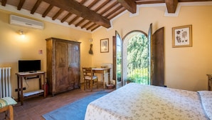 Ein Schlafzimmer mit Bett, Holzmöbeln, einem Schreibtisch und Blick durch eine offene Tür.