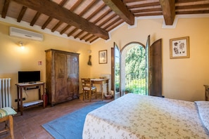Un dormitorio con cama, muebles de madera, un escritorio y vistas a través de una puerta abierta.