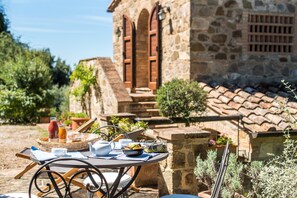 Una mesa puesta al aire libre con alimentos para el desayuno, un edificio de piedra con ventanas de arco en el fondo.