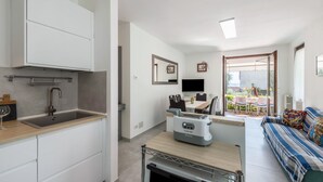 A compact kitchen with a built-in oven, a dining area with a table and chairs, and a sofa with a colorful cushion. - Holiday Apartment "Casetta - New Lake" with Private Terrace & Wi-Fi (Gardone Riviera)
