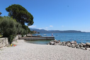 A pebbled beach with a dock, boats, and a rocky shoreline.