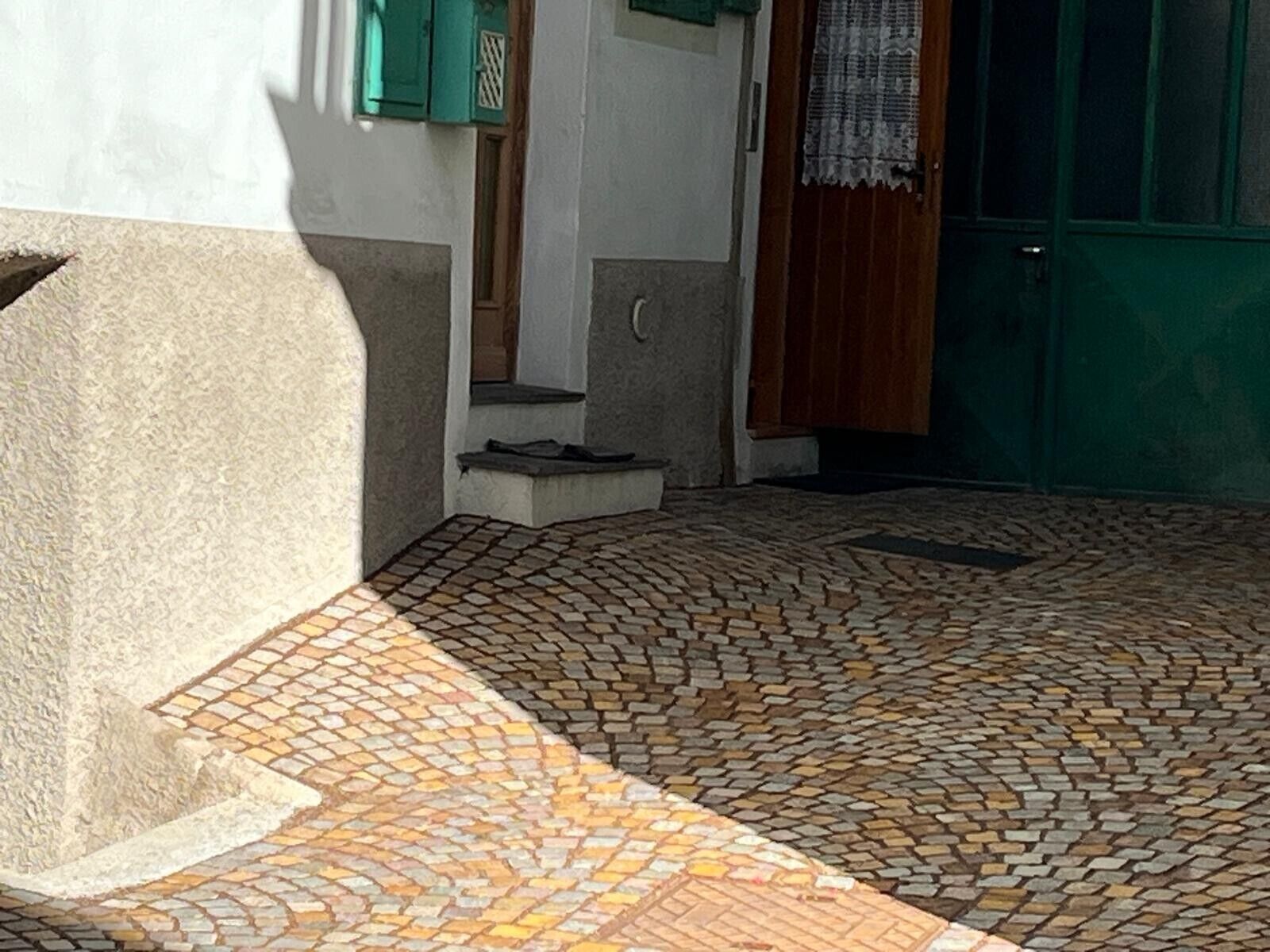 A courtyard with a patterned tile floor, a concrete bench, and a green door.
