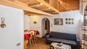 Una habitación con techo de madera, un comedor con mantel rojo, un sofá gris y una pared con cuadros enmarcados.