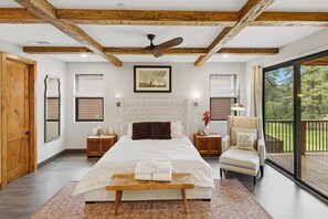 Un dormitorio con una cama grande, vigas de madera, un ventilador de techo, una ventana con persianas y vistas al exterior.