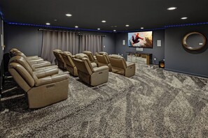 A home theater room with reclining leather chairs, a large flat-screen TV, and a carpeted floor.