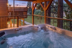 Un jacuzzi en una terraza de madera con vistas a un jardín ajardinado y árboles.