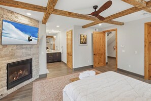 A bedroom with a fireplace, a large bed, wooden beams, and a ceiling fan.