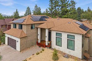 Una casa de dos pisos con techo inclinado, paneles solares, un garaje y un porche pequeño.
