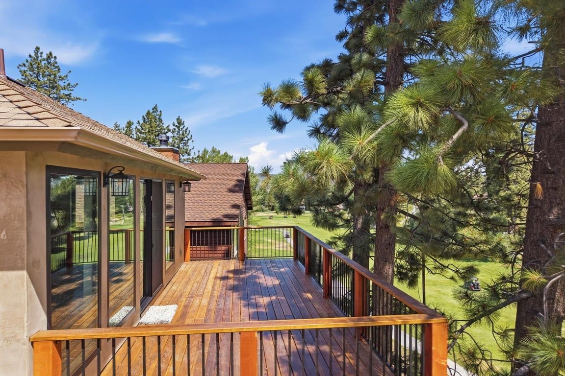 A wooden deck with a railing, overlooking a grassy area with pine trees.