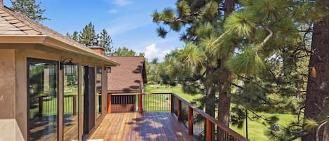 A wooden deck with a railing, overlooking a grassy area with pine trees.
