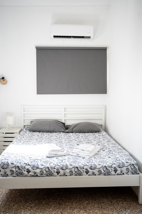 Une chambre à coucher comprenant un lit, une table de chevet, une lampe et un appareil de climatisation.