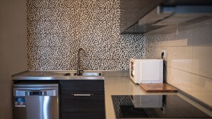 A modern kitchen with a stainless steel dishwasher, a built-in oven, and a microwave. - Apartment "Casa na Vila T2" with Shared Terrace & Wi-Fi (Fuseta)
