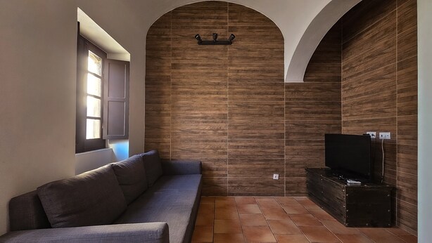 A modern living room with a sofa, TV, and wooden wall paneling. - Apartment "Casa na Vila T2" with Shared Terrace & Wi-Fi (Fuseta)