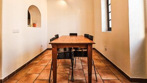 A dining room with a wooden table and chairs, a small window, and a wall-mounted light fixture. - Apartment "Casa na Vila T2" with Shared Terrace & Wi-Fi (Fuseta)