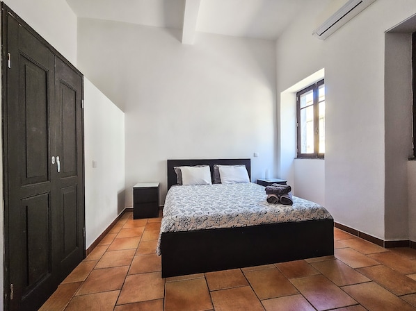 A bedroom with a bed, a nightstand, a window, and a dark wardrobe.
