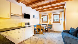 Una cocina compacta con comedor, vigas de madera en el techo, un televisor y un sofá.