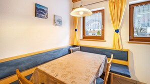 Una habitación con una mesa y banco, una lámpara colgante y un ventanal con cortinas.