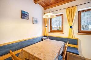 Una habitación con una mesa y banco, una lámpara colgante y un ventanal con cortinas.