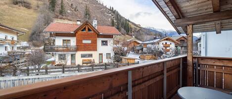 Ein Holzbalkon mit Tisch, mit Blick auf ein Dorf mit traditionellen Häusern und einem Berg im Hintergrund.