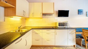 Una cocina con armarios blancos, un microondas y un televisor en la pared.