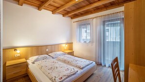 A bedroom with two beds, wooden headboard, bedside lamps, a wooden chair, and a window with sheer curtains. - Apartment 'Speckign  3' with Mountain View, Balcony and Wi-Fi (Ahrntal)