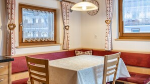 A room with a table, chairs, a bench, a window with curtains, a clock, and a wall-mounted light fixture. - Apartment 'Speckign  3' with Mountain View, Balcony and Wi-Fi (Ahrntal)