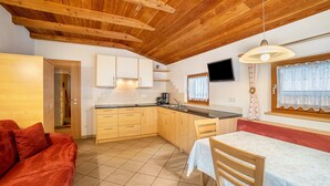A compact kitchen with wooden cabinets, a dining table, and a red sofa. - Apartment 'Speckign  3' with Mountain View, Balcony and Wi-Fi (Ahrntal)