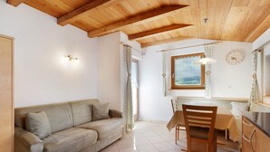 A room with a wooden ceiling, a sofa, a dining table with chairs, a clock, and a window with curtains. - Apartment 'Speckign  2' with Mountain View, Balcony and Wi-Fi (Ahrntal)