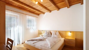 A bedroom with a wooden bed, bedside tables, a wooden desk, and a window with sheer curtains. - Apartment 'Speckign  2' with Mountain View, Balcony and Wi-Fi (Ahrntal)