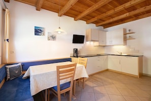 A kitchen with a dining area, wooden ceiling beams, a television, and a tiled floor.