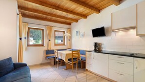 Una habitación con techo de madera, una mesa de comedor con sillas, un sofá, una zona de cocina con armarios y un televisor.