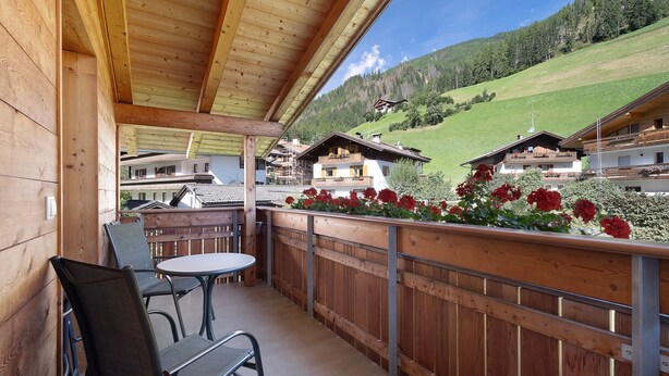 Un balcón de madera con una mesa y sillas, con vistas a un paisaje montañoso.